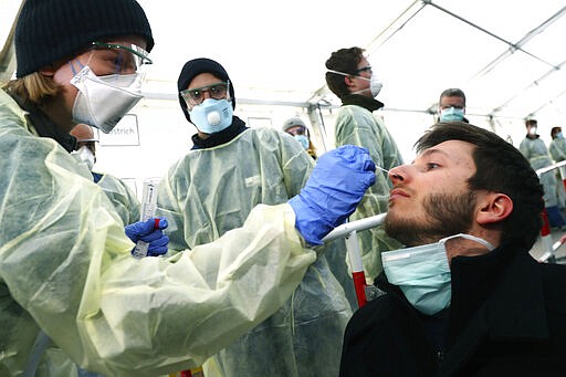 FILE - In this March 23, 2020, file photo, medical employees demonstrate testing, at a coronavirus test center for public service employees, during a media presentation in Munich, Germany. Labs were quick to ramp up their testing capacity and now experts say up to 500,000 tests can be conducted in Germany per week. That quick work, coupled with the country's large number of intensive care unit beds and its early implementation of social distancing measures, could be behind Germany's relatively low death toll.  (AP Photo/Matthias Schrader, File)