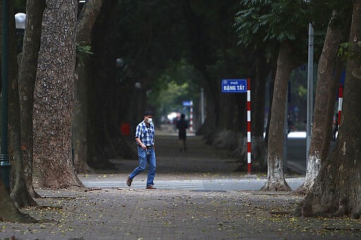 A man wearing a face mask walks on a quiet street in Hanoi, Vietnam, Wednesday, April 1, 2020. Vietnam on Wednesday starts two weeks of social distancing to contain the spread of COVID-19. The new coronavirus causes mild or moderate symptoms for most people, but for some, especially older adults and people with existing health problems, it can cause more severe illness or death. (AP Photo/Hau Dinh)