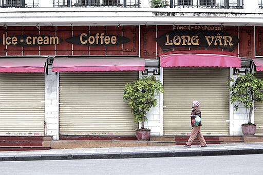 A woman walks past a closed cafe in Hanoi, Vietnam, Wednesday, April 1, 2020. Vietnam on Wednesday starts two weeks of social distancing to contain the spread of COVID-19. The new coronavirus causes mild or moderate symptoms for most people, but for some, especially older adults and people with existing health problems, it can cause more severe illness or death. (AP Photo/Hau Dinh)