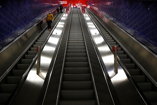 FILE - In this March 30, 2020, file photo, a woman wears a face mask as she rides an empty escalator in Munich, Germany. Labs were quick to ramp up their testing capacity and now experts say up to 500,000 tests can be conducted in Germany per week. That quick work, coupled with the country's large number of intensive care unit beds and its early implementation of social distancing measures, could be behind Germany's relatively low death toll.  (AP Photo/Matthias Schrader, File)