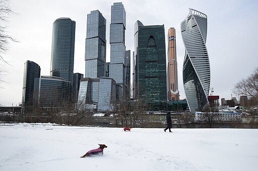 A woman walks her dogs with Moscow City skyscrapers in the background in Moscow, Russia, Tuesday, March 31, 2020. The Russian capital has woken up to a lockdown obliging most people in the city of 13 million to stay home. The government ordered other regions of the vast country to quickly prepare for the same as Moscow, to stem the spread of the new coronavirus. The new coronavirus causes mild or moderate symptoms for most people, but for some, especially older adults and people with existing health problems, it can cause more severe illness or death. (AP Photo/Pavel Golovkin)