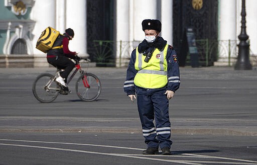 A food delivery courier rides a bike past a road police officer wearing face mask, to protect against coronavirus,  in St.Petersburg, Russia, Tuesday, March 31, 2020. Moscow, the country's capital, and more than 30 Russian regions have been on lockdown since Monday, with most businesses closed and residents not allowed to leave their apartments except for grocery shopping, buying medicines, taking out trash or walking their dogs. The new coronavirus causes mild or moderate symptoms for most people, but for some, especially older adults and people with existing health problems, it can cause more severe illness or death. (AP Photo/Dmitri Lovetsky)