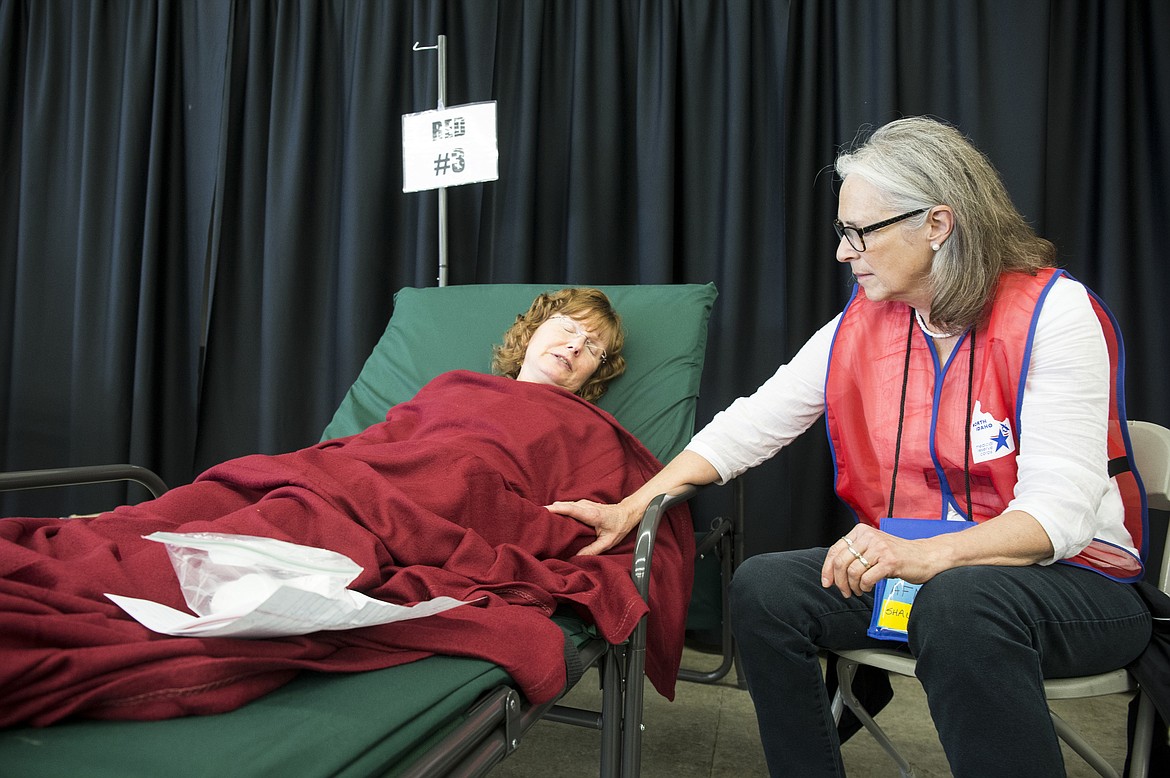 LOREN BENOIT/Hagadone News Network
Volunteer Shauna Miller, right, of the Medical Reserve Corps, comforts Audrey Hammons at her bed at a medical needs shelter at the fairgrounds on Thursday for evacuees of the fictional tsunami and earthquake disaster that  devastated the West Coast.