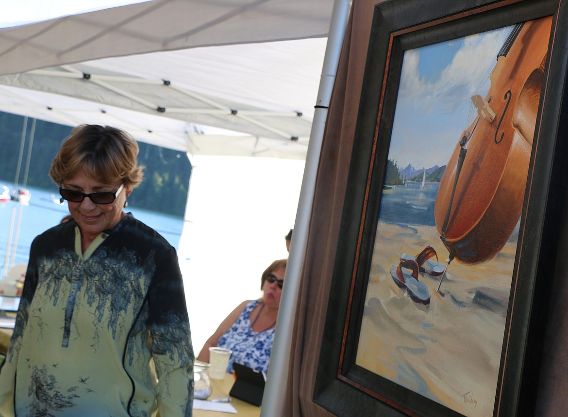 (Photo by CAROLINE LOBSINGER)
Kathryn Weisberg, a Sandpoint artist and conservationist best known for her paintings of wildlife and impressionist landscapes, unveils the poster she created for the Festival at Sandpoint&#146;s 34th season of the summer concert series. Weisberg, who was chosen by a committee of her artistic peers, made up of the Festival&#146;s past poster artists to create a piece of original artwork for the Festival at Sandpoint, said she came up with the idea for her painting after imagining what it would be like to be a musician trapped inside practicing. Finally, the chellist, grabs her instrument and embeds it in the sand and begins to practice outside so as to enjoy the community&#146;s beauty.