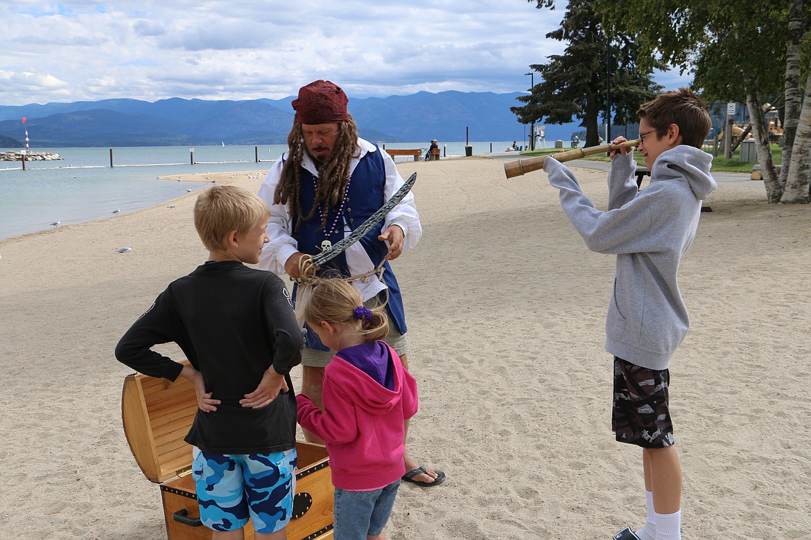 &#151; Photo by MARY MALONE
David Muhly, 11, of Coeur d'Alene, right, looks through a spyglass loaned to him from Captain Dan Mimmack, top center. David's siblings, 9-year-old Nathaniel and 4-year-old Rebecca are getting ready to &quot;plunder&quot; Mimmacks treasure chest on City Beach in Sandpoint Thursday.