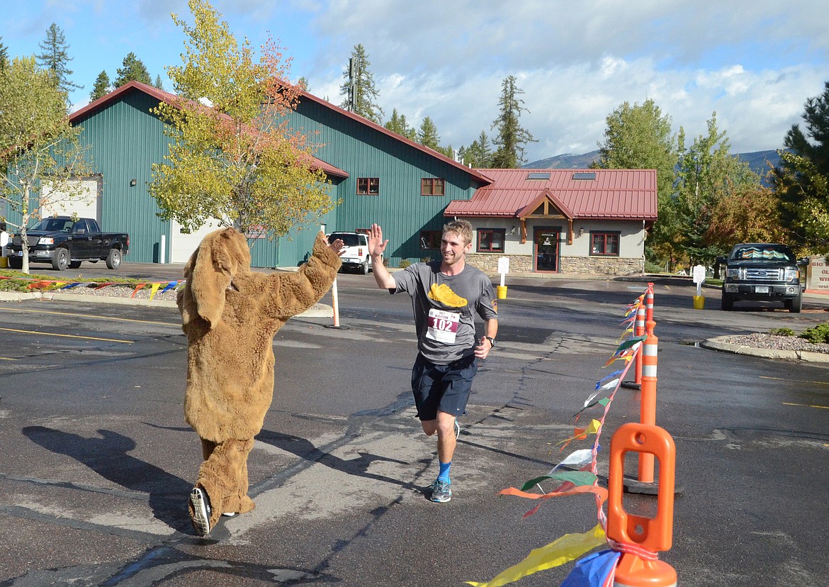 Drew Adams of Spokane, Washington, gets a high-five from a bear as he finishes the half marathon Sunday in the Two Bear Marathon. Heidi Desch / Whitefish Pilot