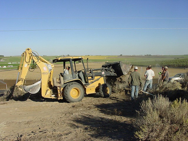 Ted Escobar/The Sun Tribune - Project Manager Mark Anderson operates Ryan Christensen&#146;s backhoe, assisted by the Sagebrush Crew.