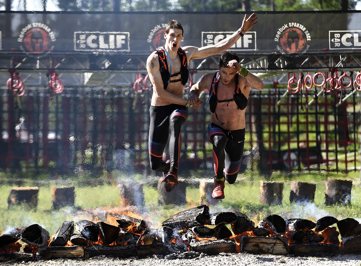 Ian Hose, left, and Matt Kempson jump over a fire at the finish line to win the Montana Spartan Beast together at Averill's Flathead Lake Lodge on Saturday. Kempson waited for Hose so they could finish together. (Aaric Bryan/Daily Inter Lake)