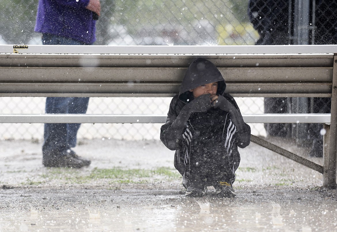 Carson Gulick, 9, takes shelter from the hail underneath a bench while watching Glacier at the Montana AA Softball Championship at the Conrad Complex on Thursday. The game had to be postponed. (Aaric Bryan/Daily Inter Lake)