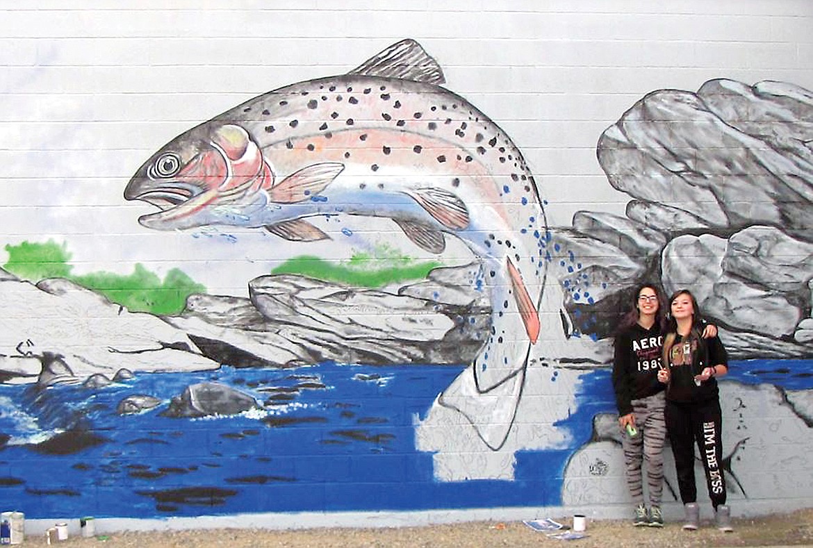 Students Alisha Brooks and Ali Johnson under the supervision of Todd Berget, painting the 30th public mural in Libby in October, 2016. Once the mural was finished, the students signed their names at the bottom. (photo courtesy of Todd Berget)