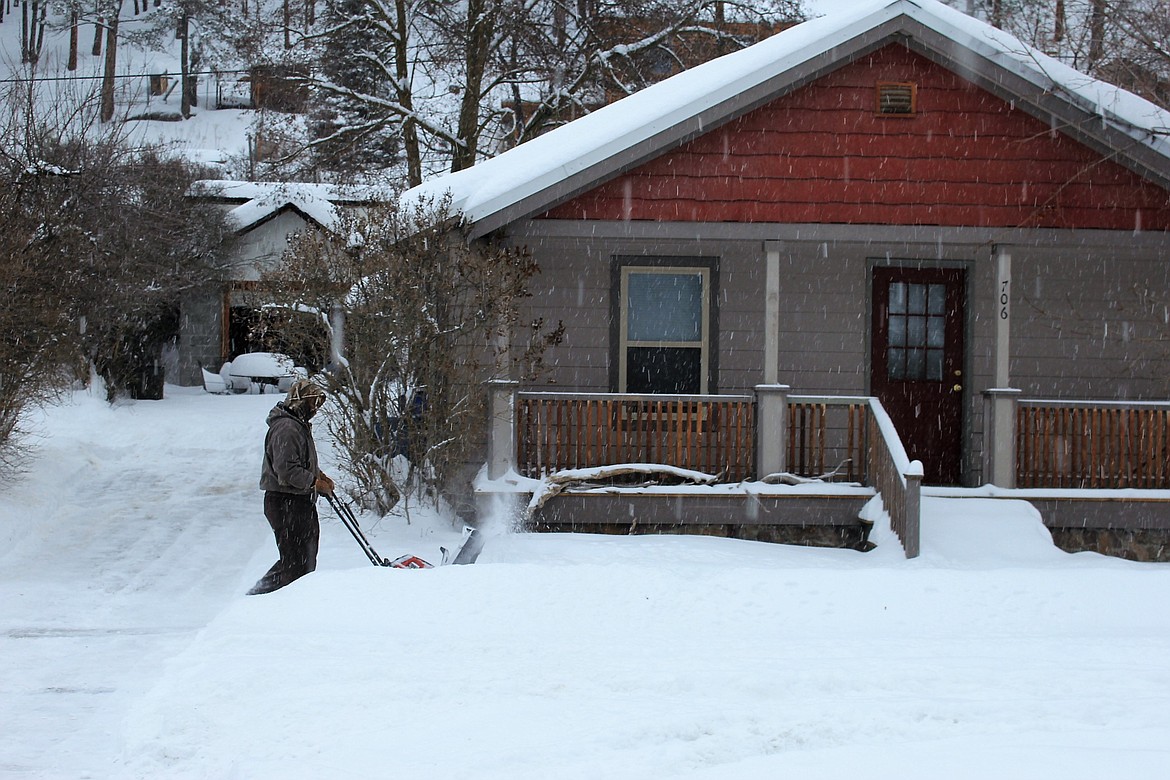 An Alberton homeowner clears the sidewalk as snow continues to blanket the area during Monday&#146;s snowstorm. (Kathleen Woodford photos/Mineral Independent).