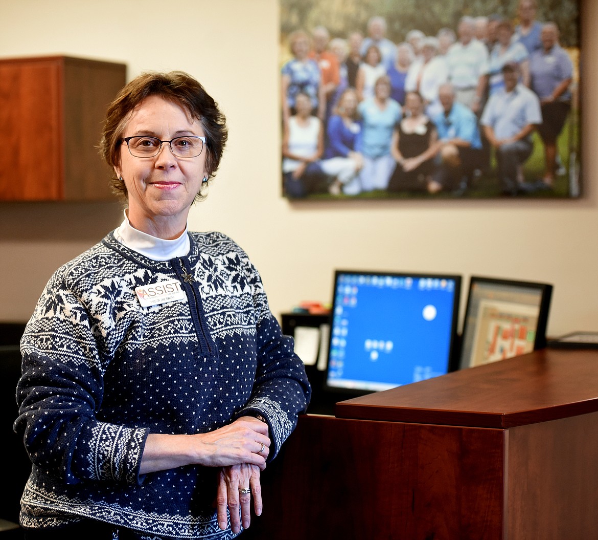 Jane Emmert is the director at ASSIST in Kalispell. In the background is a group photo of ASSIST volunteers.