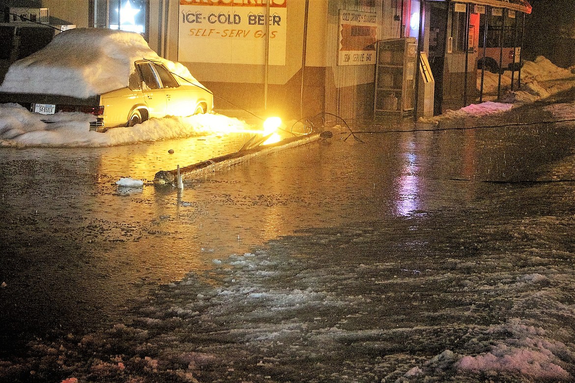 A lamp pole lies in a pool of water as heavy rain and melting snow crease a large puddle in front of the Valley Grocery in Alberton on Thursday evening. (Kathleen Woodford/Mineral Independent).