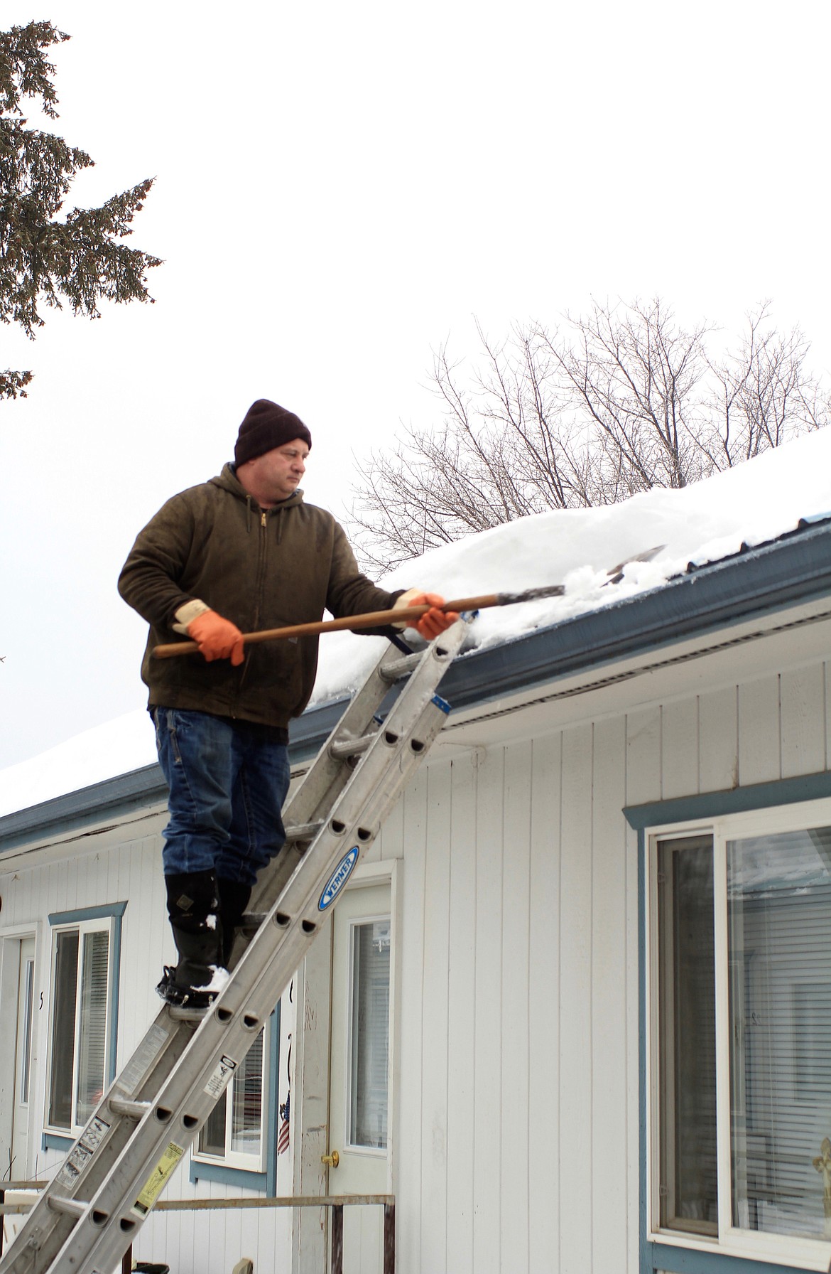 JOHNNY BUCKNER shovels off snow and ice from the roof of several apartments located on Meany Street in Plains on Feb. 9, as rain was falling. (Douglas Wilks/Clark Fork Valley Press)