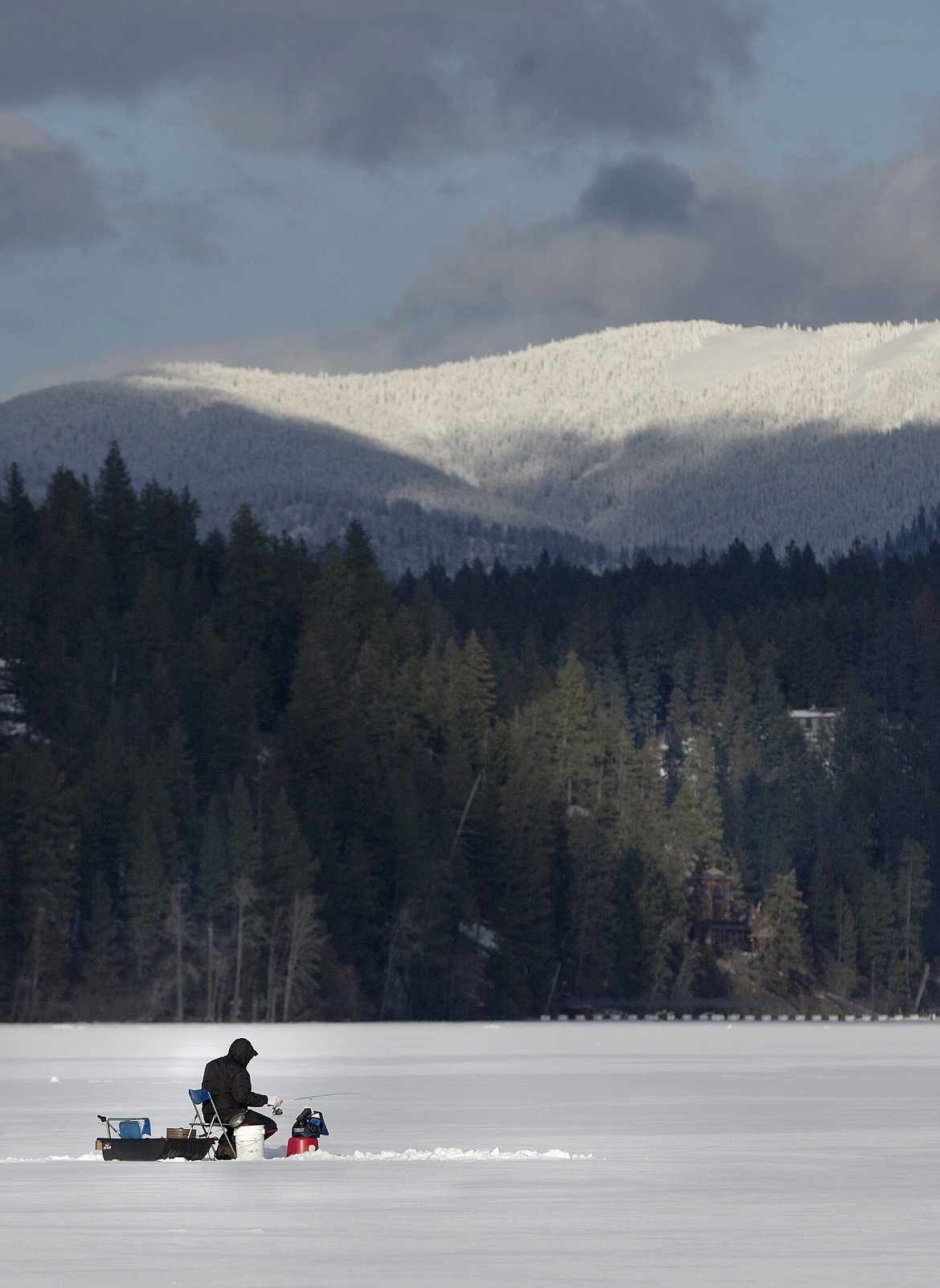 A lone ice fisherman finds a spot away from a cluster of others ice fishing.