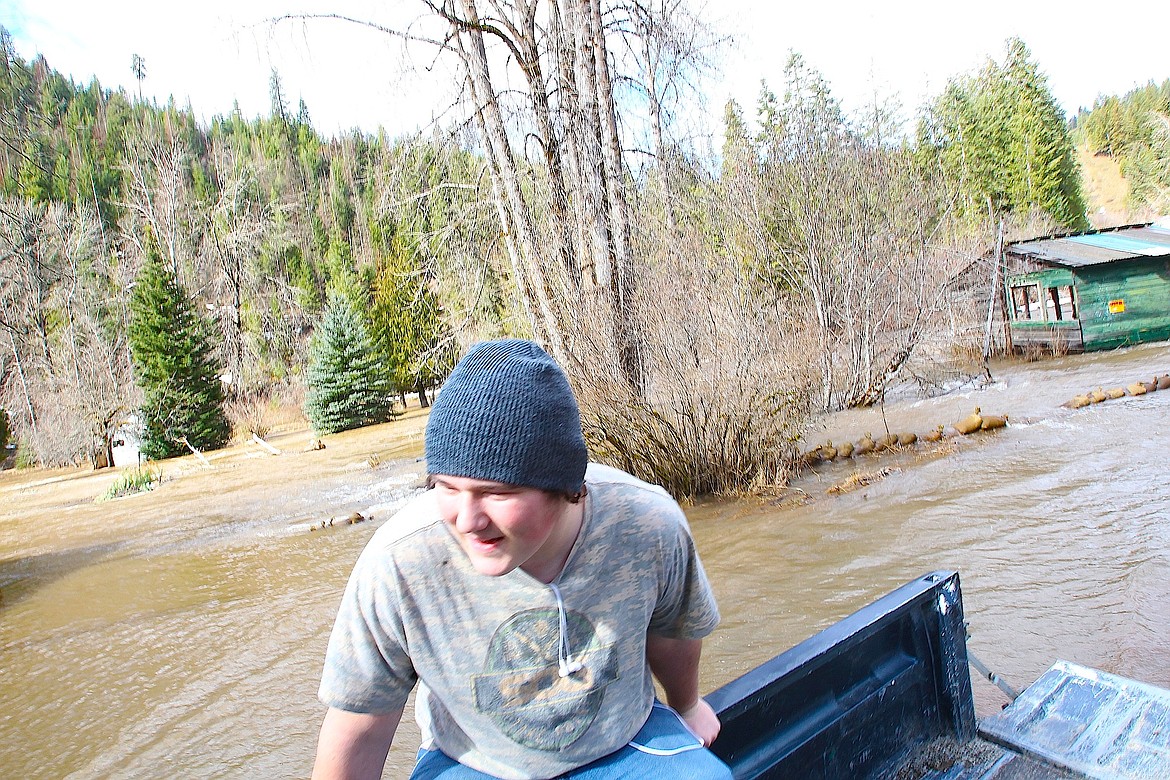 BRIAN WALKER/Press
Brenden Byrne rides in the back of a truck en route to fill more sandbags on Thursday. A flooded Wolf Lodge Creek in the background shows water flowing over a flood berm.