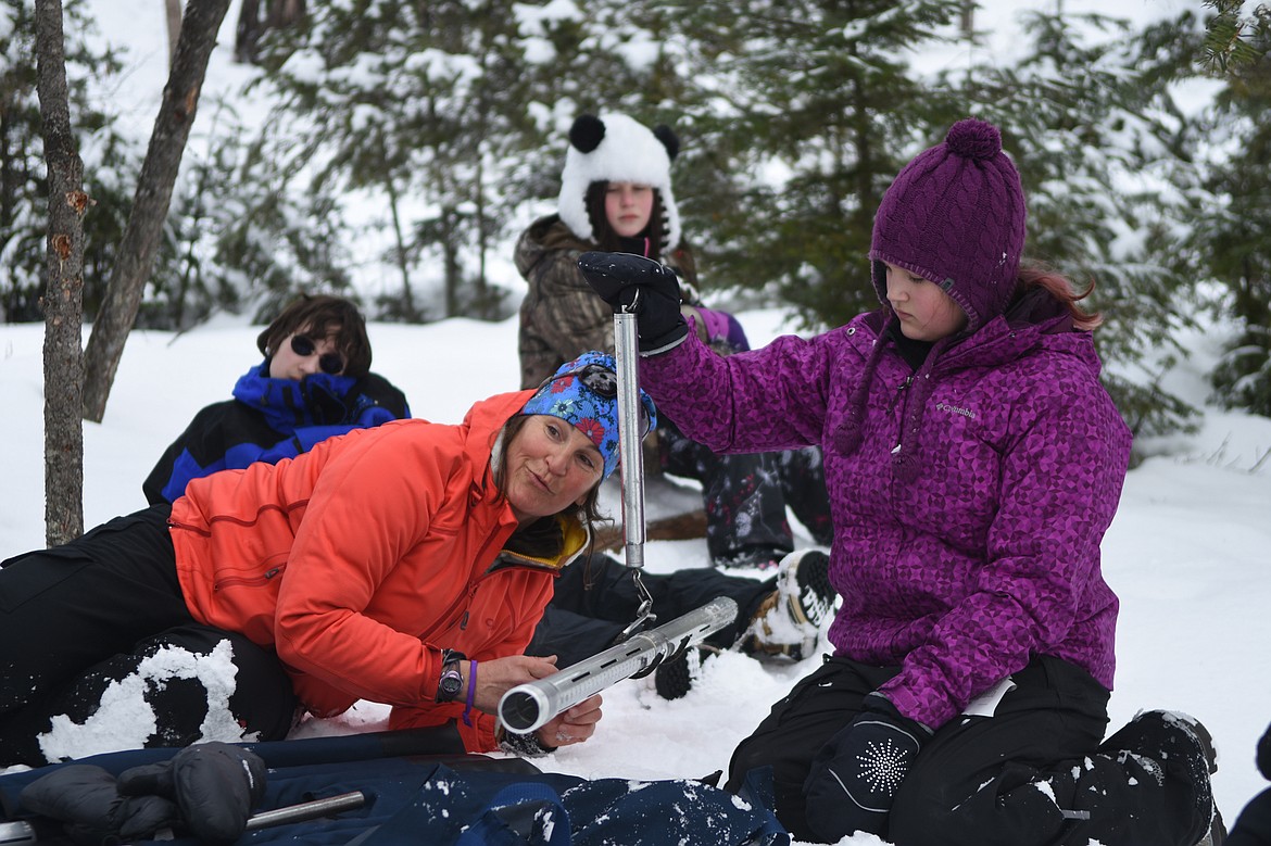 Kim Corette explains how to check snow depth while student Jessica Williamson holds a scale. (Daniel McKay photos/Whitefish Pilot)