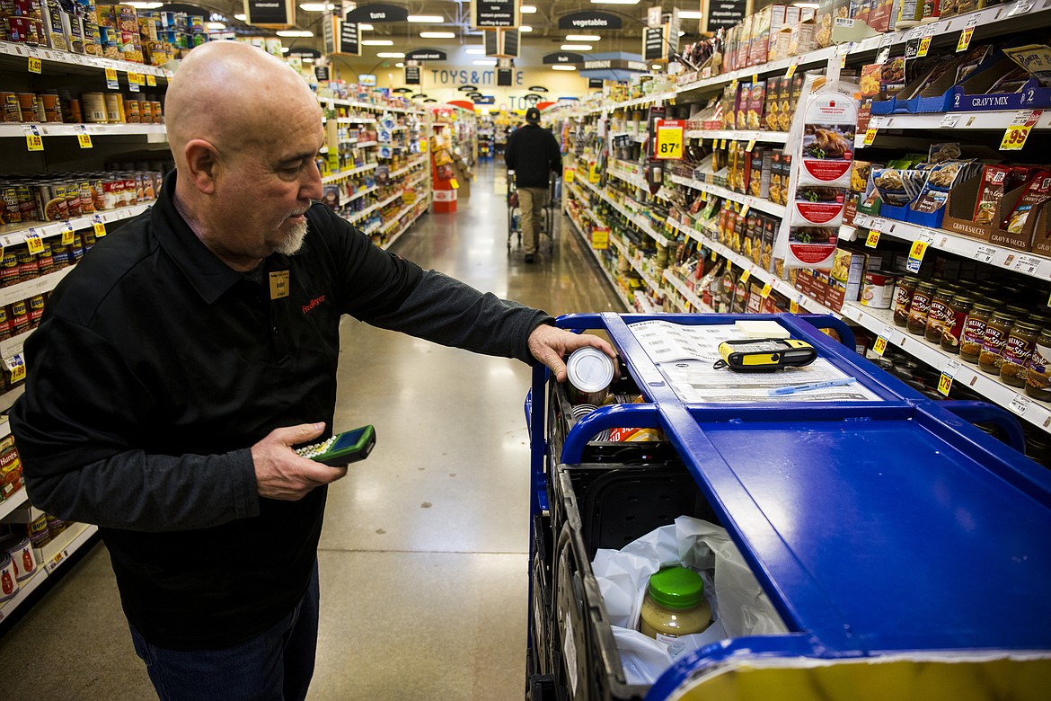 LOREN BENOIT/PressFred Meyer employee Manny Tavison places a can of soup into a ClickList container Wednesday afternoon. Tavison and other ClickList workers have to juggle multiple orders as they go up and down grocery aisles.