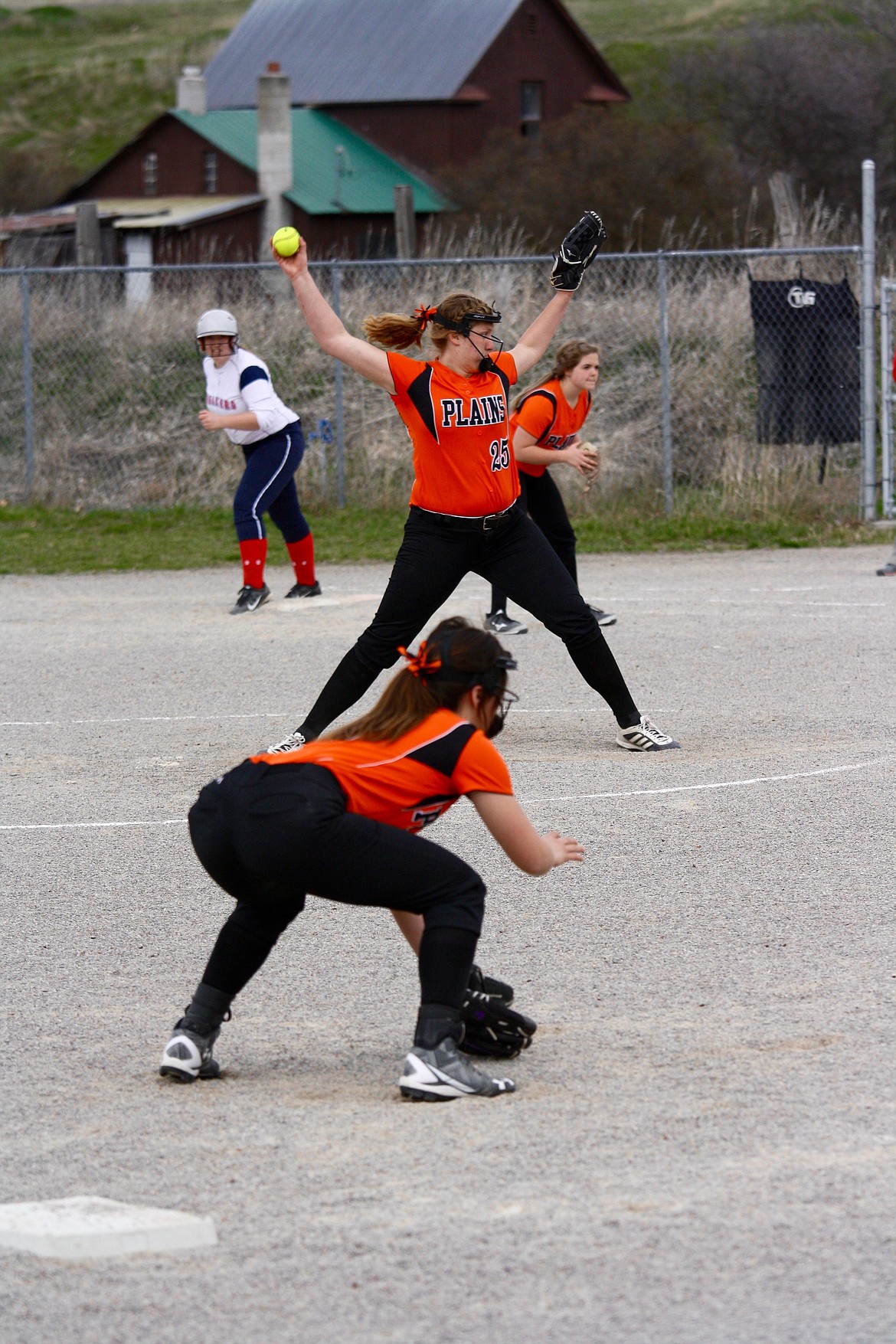 JESSICA THOMPSON (#25) of the Plains/Hot Springs Trotters fastpitch softball team winds up for a pitch with a Loyola runner on first. Third base and first base players are ready for any hit. (Douglas Wilks photos/Clark Fork Valley Press)