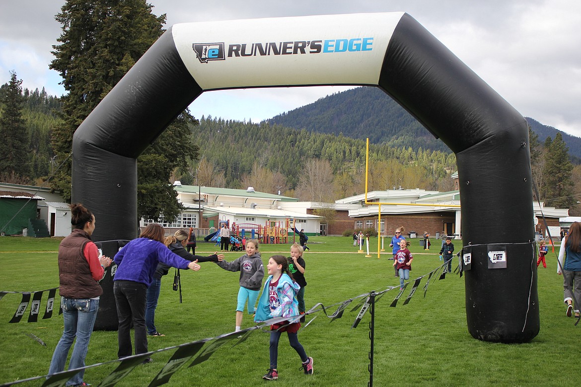 Barb Jaspers stands at the finish line and gives students a high-five as they complete the 1-mile and 5K races during Tuesday&#146;s Annual Mineral County Fun Run. (Kathleen Woodford/Mineral Independent).