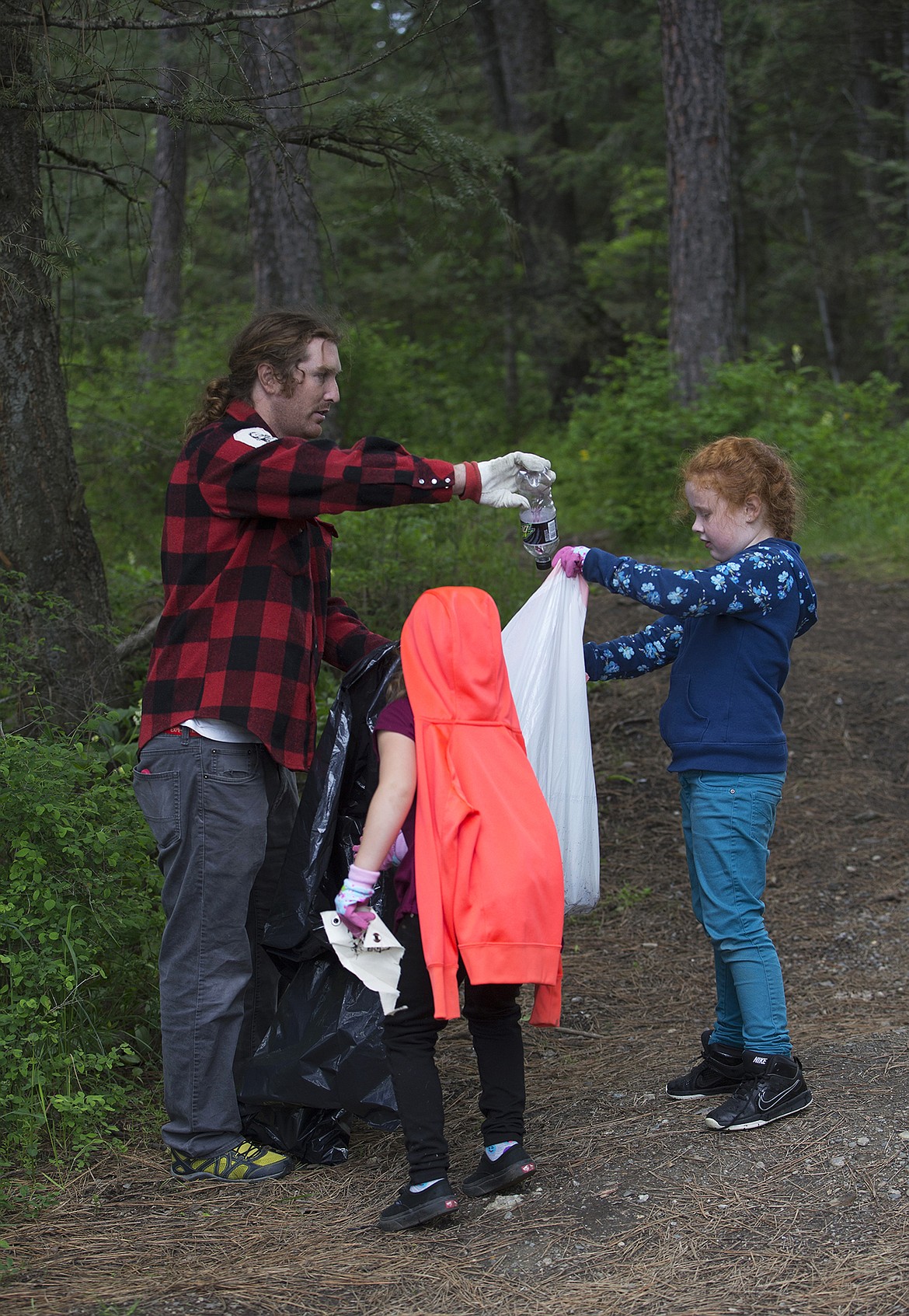 LISA JAMES/Press
Local environmental activist Dylan Stiegemeier disposes of glass recyclables as John Brown Elementary School first-graders Hazel Nutterville, right, and Casey Slokum, hold the bag during a litter cleanup in the woods near their school on May 18.