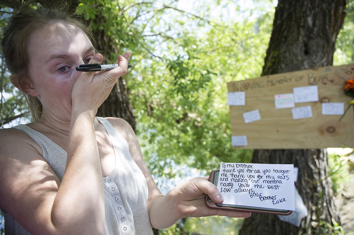 LISA JAMES/PressSarah Holbrook writes a note for her sister's dog, Bear, from her sister's younger dog Luke, at Hayden Lake Tuesday. Bear drowned in the lake Monday after being pulled down against a drainage grate.