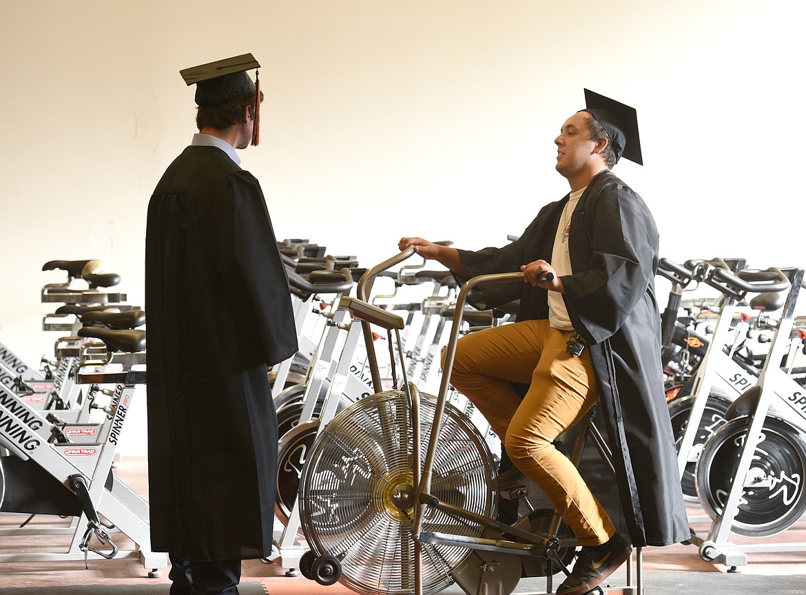 Flathead graduate Jaycob Serrano rides a stationary bike and Michael Miller stands in front of the fan as the two wait in the school's weight room before the 2017 Commencement Ceremony on Friday. (Aaric Bryan/Daily Inter Lake)