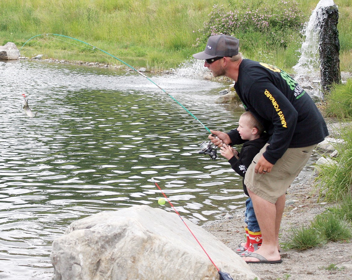 James Schreiner helps his son, James Jr., 2, reel in a trout at Troy fishing pond on Saturday. (Elka Wood/The Western News)