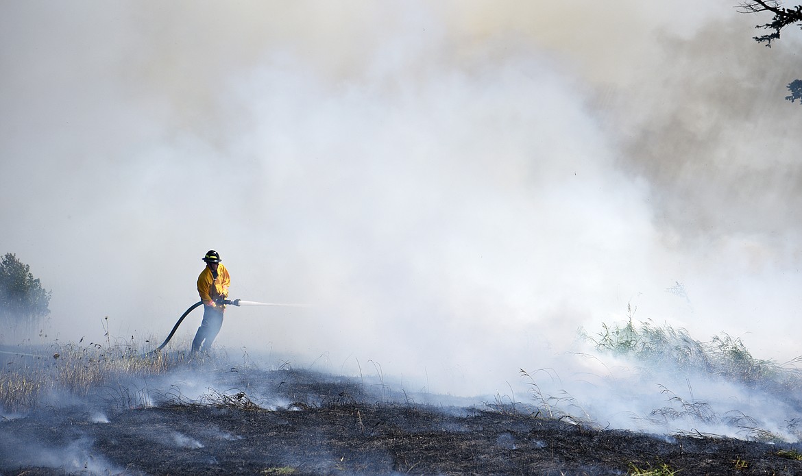 A firefighter sprays water on a grass fire on Appleway drive in Kalispell on Thursday. (Aaric Bryan/Daily Inter Lake)