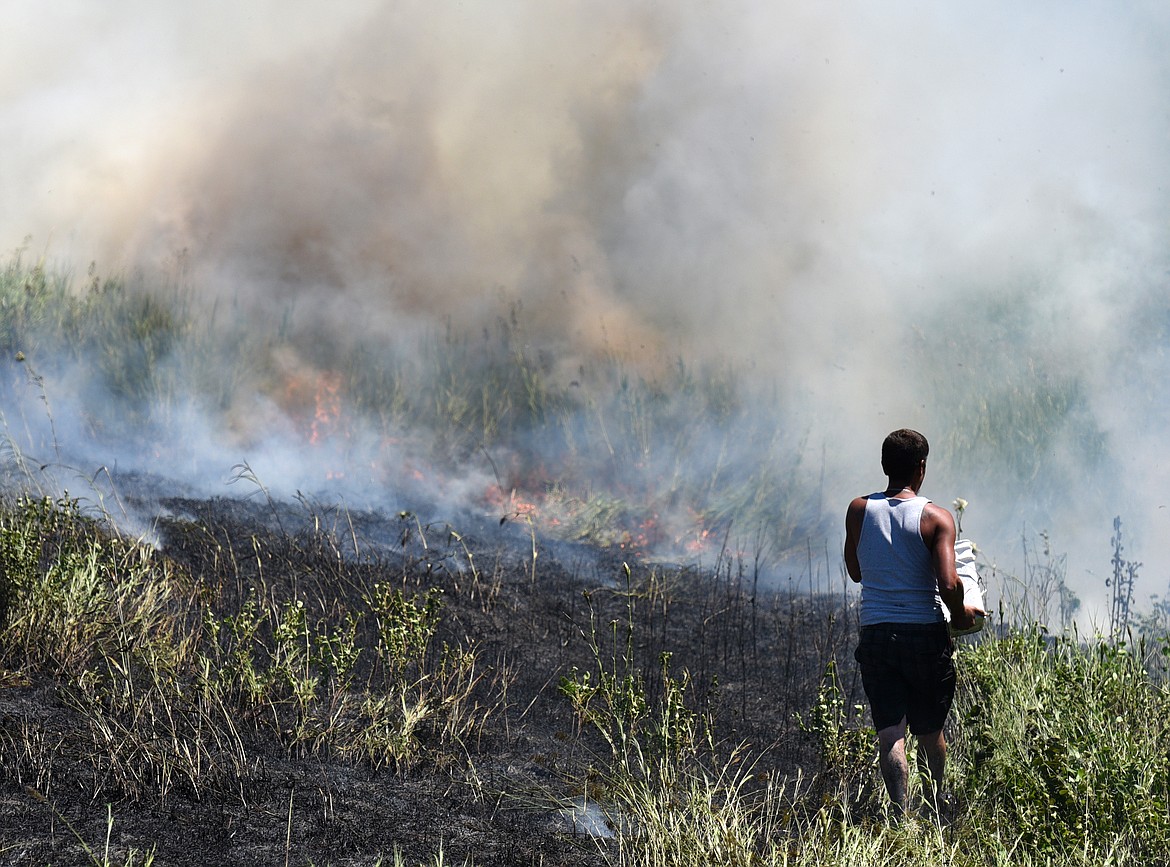 A bystander throws a bucket of water on the grass fire on Appleway Drive in Kalispell on Wednesday. (Aaric Bryan/Daily Inter Lake)