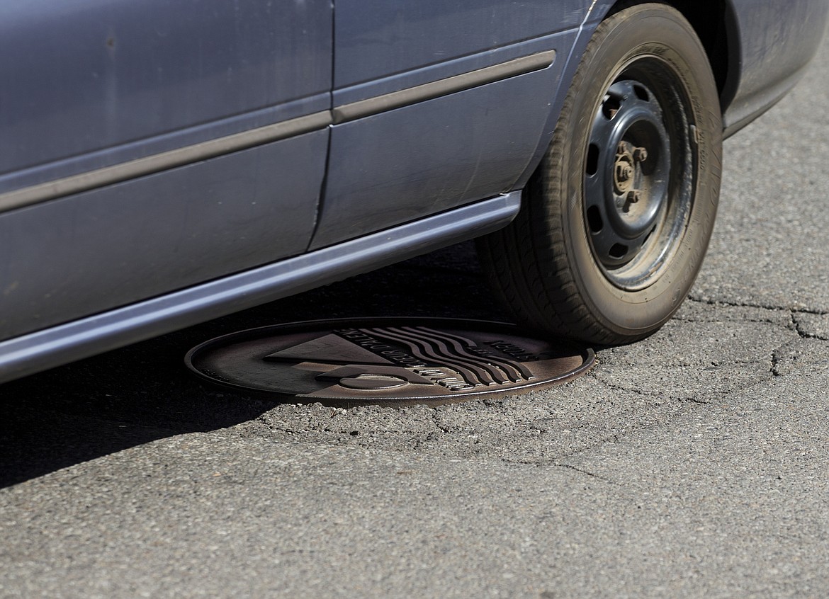 LOREN BENOIT/Press
A vehicle drives over an uneven manhole on Fourth Street in downtown Coeur d'Alene on Monday. Square-cut manhole cover repairs &#8212; called diamond cuts &#8212; have a tendency to sink or expand, causing bumps in city streets. The city plans a pilot project this summer to use round cuts, which will be level with the street and should eliminate the bumps of driving over sewer manholes.