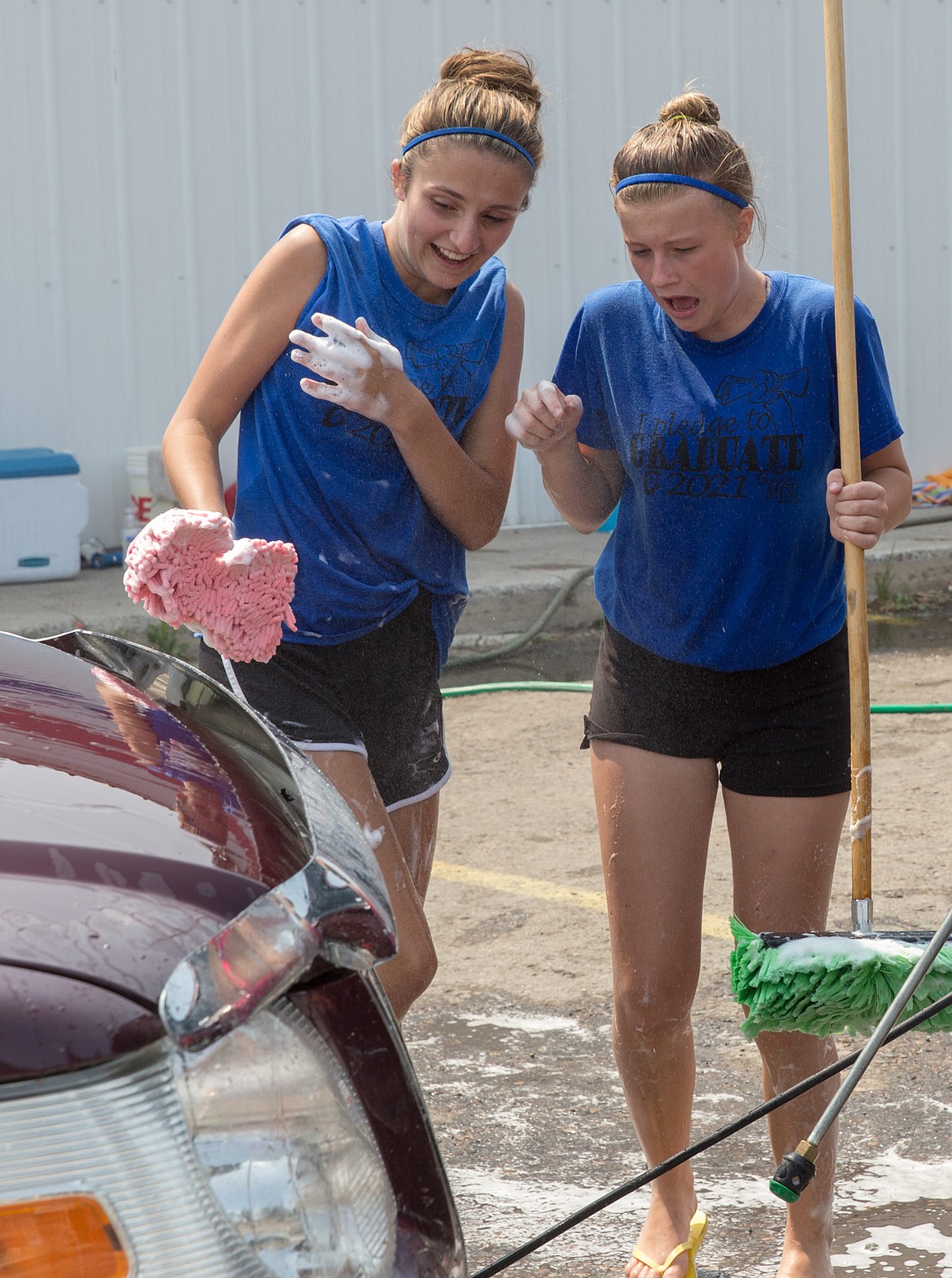 Aspen Swartzenberger, left, and Aren James react to a large dead insect stuck in a car&#146;s grill as Shelya Gallagher prepares to spray a car with water in front of Carquest Auto Parts in Libby Saturday, Aug. 5, 2017. They were participating in a fundraising carwash for the Libby High School volleyball team. (John Blodgett/The Western News)