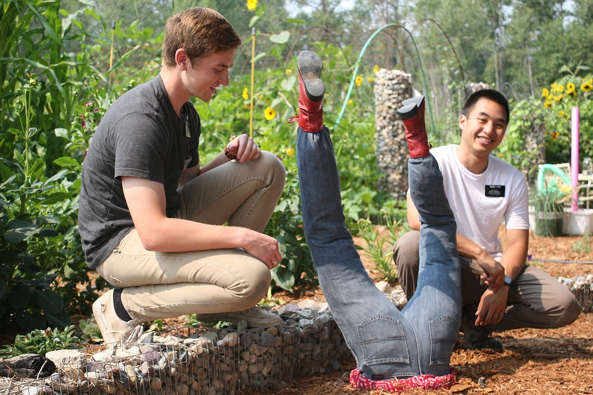 Mormon volunteers Elder King, left, and Elder Chien, right, sit with &#147;Daisy,&#148; Libby Community Garden&#146;s newest scarecrow, whom they helped make on Aug. 10. (Elka Wood/The Western News)