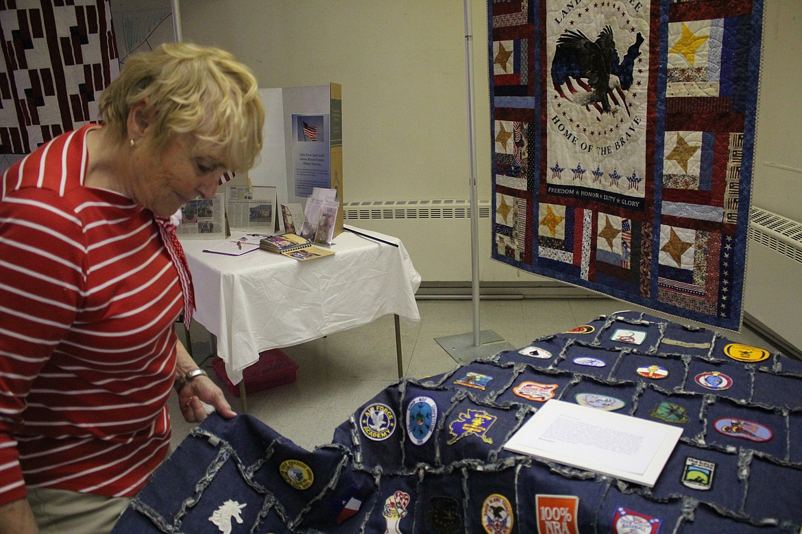 Cabin Fever Quilt member Susan Charles shows a patch quilt created by Glordine Johnson. Behind her is a quilt which will be given to a Mineral County veteran as part of their Veterans Project. (Kathleen Woodford/Mineral Independent).