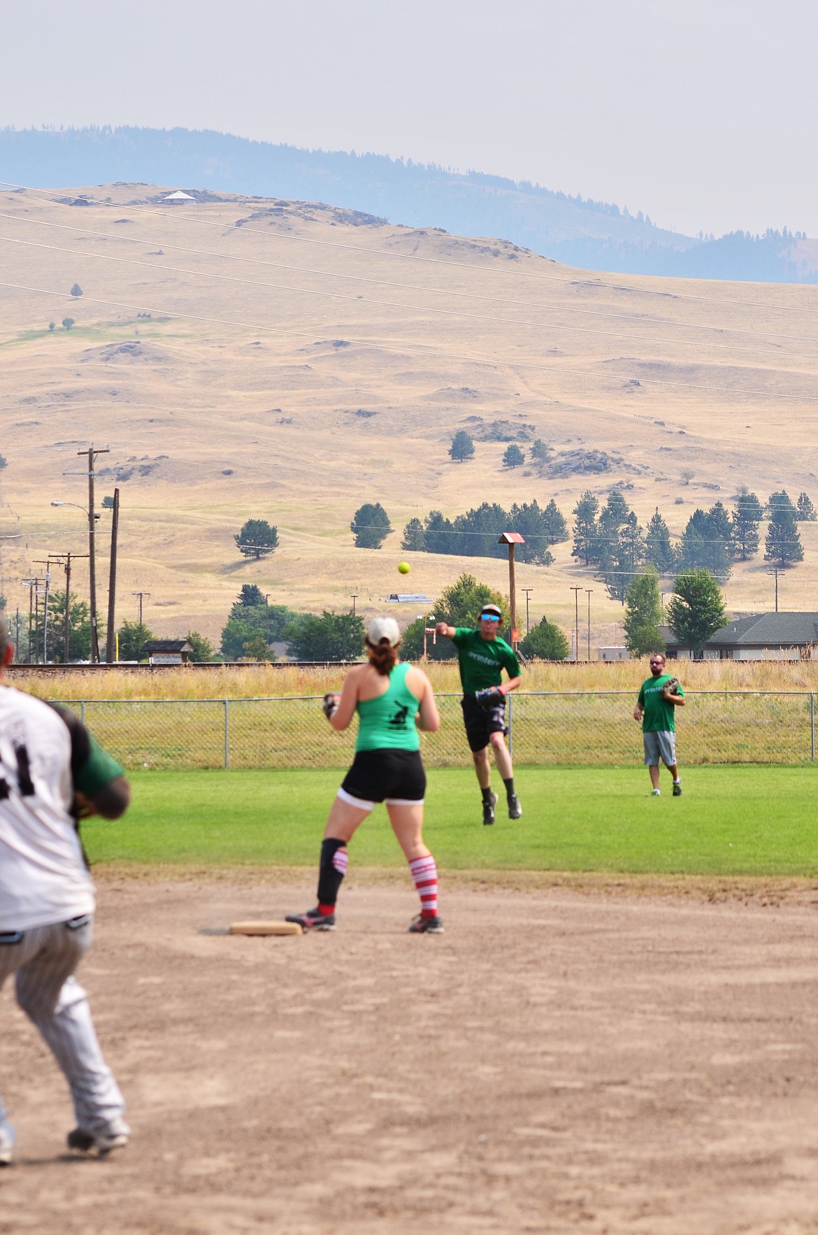 Neiman Wilson looking to advance to second, Marie Errecart playing second base, Ryan Ovitt making throw with Kevin&#160;Kegel looking on from left field.Photo Credit Erin Jusseaume Clark Fork Valley Press