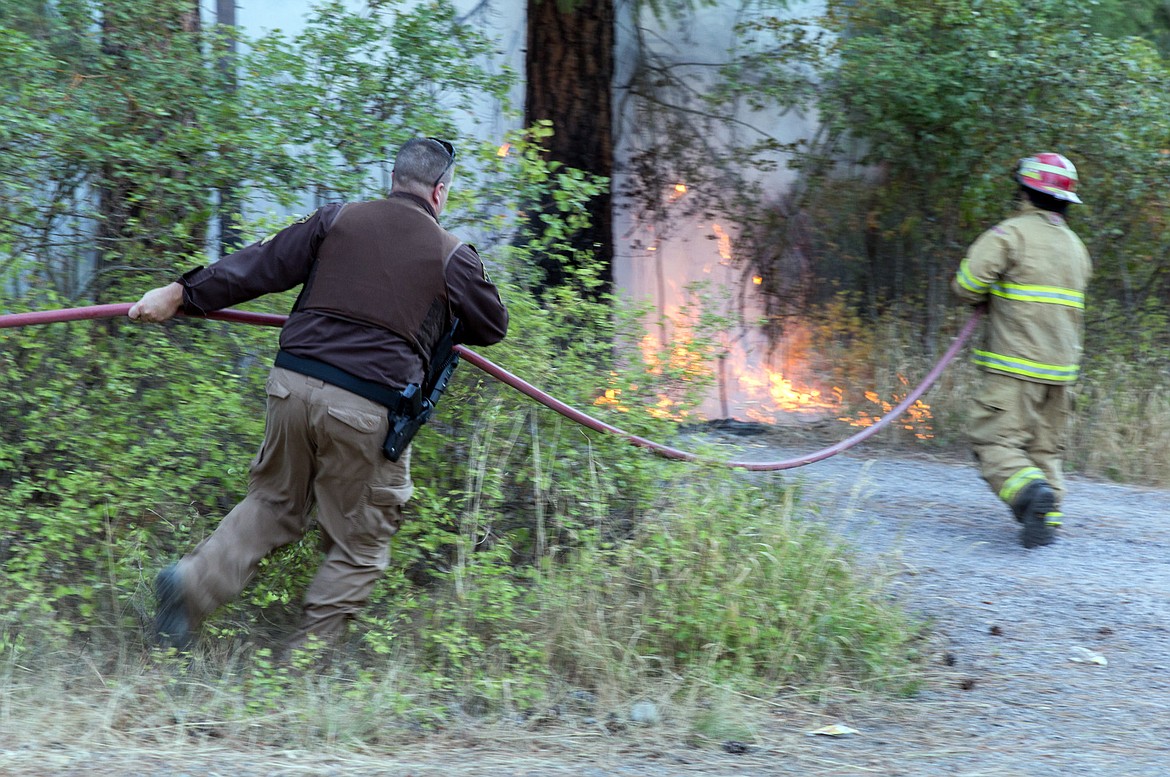 Lincoln County Sheriff&#146;s Sgt. Brandon Holzer, left, lends a hand with a hose as the Libby Volunteer Fire Department responds to a small brush fire on Park Street Saturday evening. (John Blodgett/The Western News)