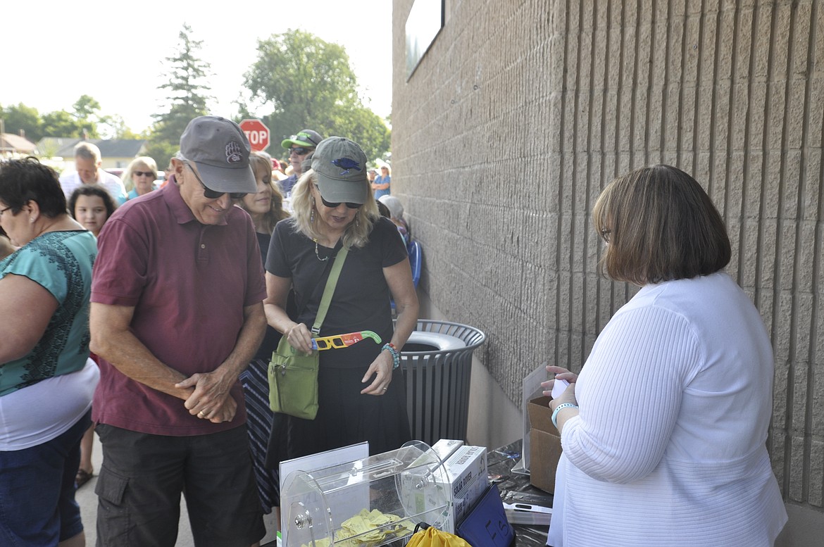 Dennis Johnson, left, stands with Joan Black as they get their special glasses for Monday&#146;s solar eclipse at the library in Polson.