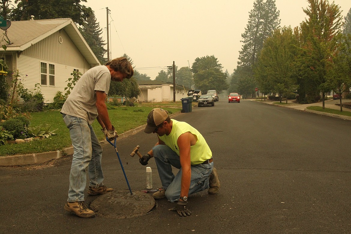 Tony Verdal, left, of Hayden Lake, and Dave Gerzina of Coeur d&#146;Alene work to clean up manhole covers in a Front Avenue intersection. Verdal and Gerzina were among those who worked in the heavy smoke Tuesday following an air-quality advisory restricting outdoor activities and recommending heavy work be avoided. &#147;It&#146;s not bugging me,&#148; Gerzina said of the smoke.