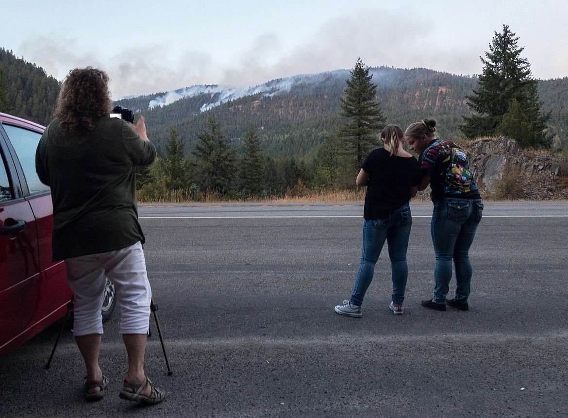 Cindy Wagner, left, Katie Brown and Bridgett Haskins, all of Libby, photograph the West Fork fire from a pullout along Highway 2 a few miles east of Libby Sunday evening. (John Blodgett/The Western News)