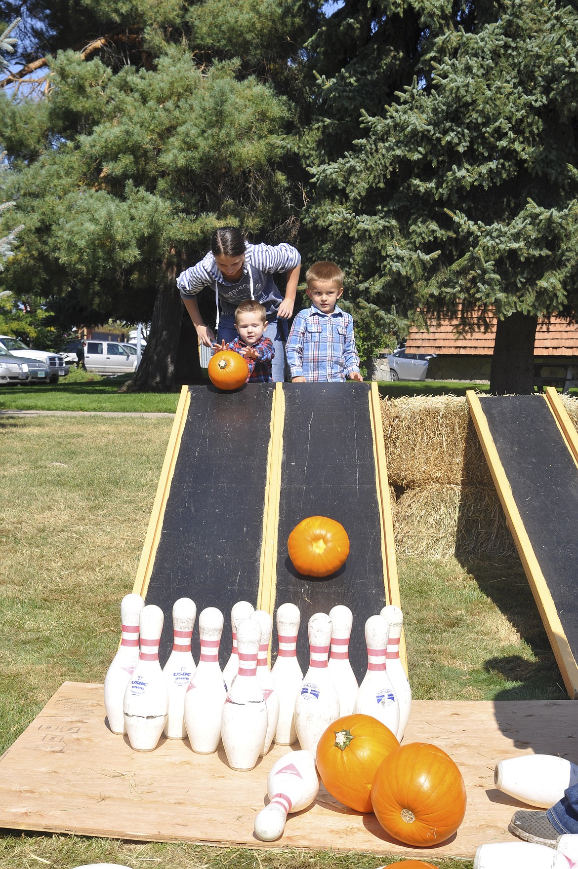 Emmett Booth, 2, left, rolls down a pumpkin to knock down pins, moments after brother Wyatt, 4, pushed his pumpkin down the ramp. Helping the brothers was their aunt, Savanah Duell. The family attended Harvest Fest in their hometown of Ronan Saturday. (Ashley Fox/Lake County Leader)