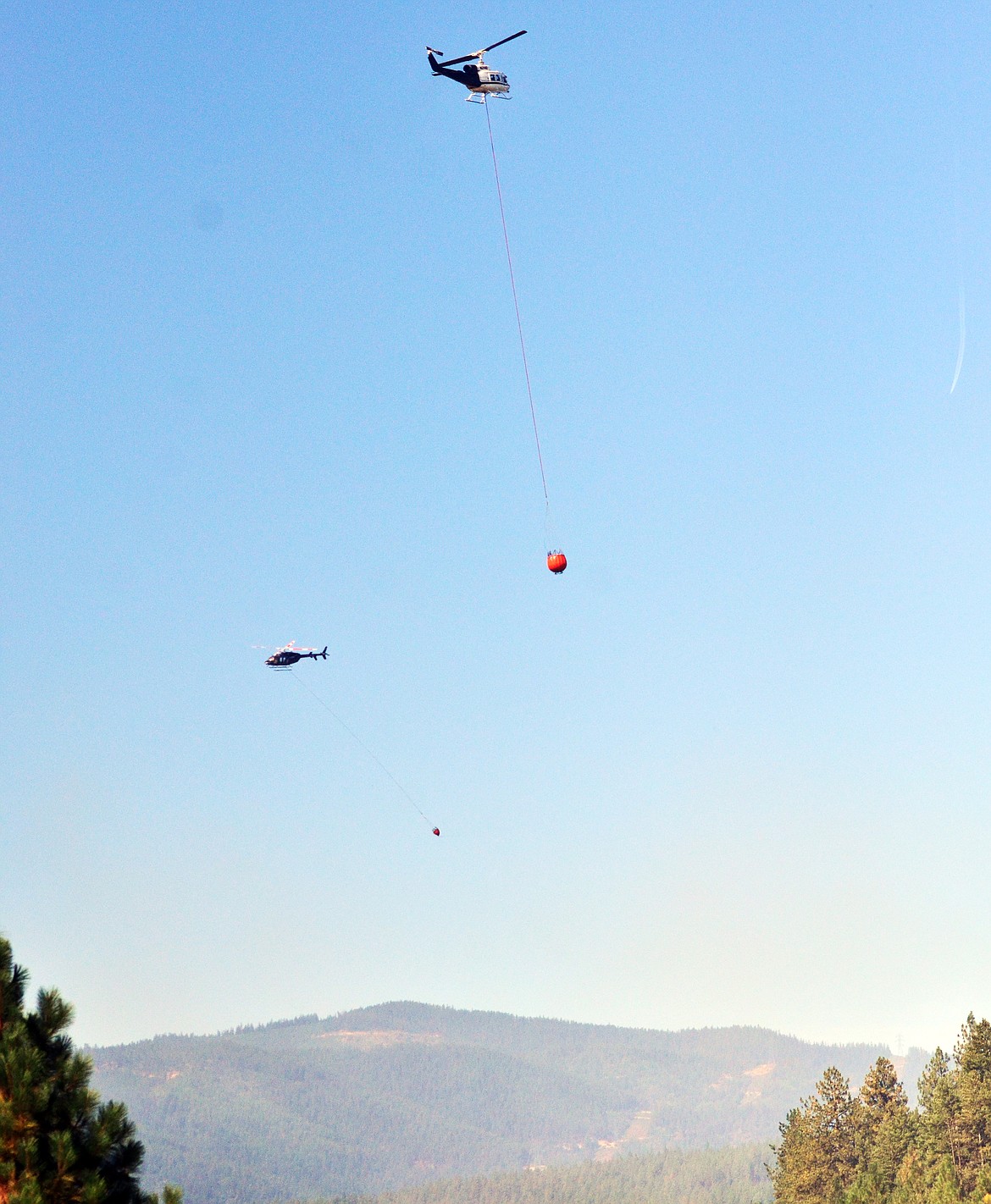 Two helicopters trading off on one fire. One dips as the other drops. (Erin Jusseaume/ Clark Fork Valley Press)