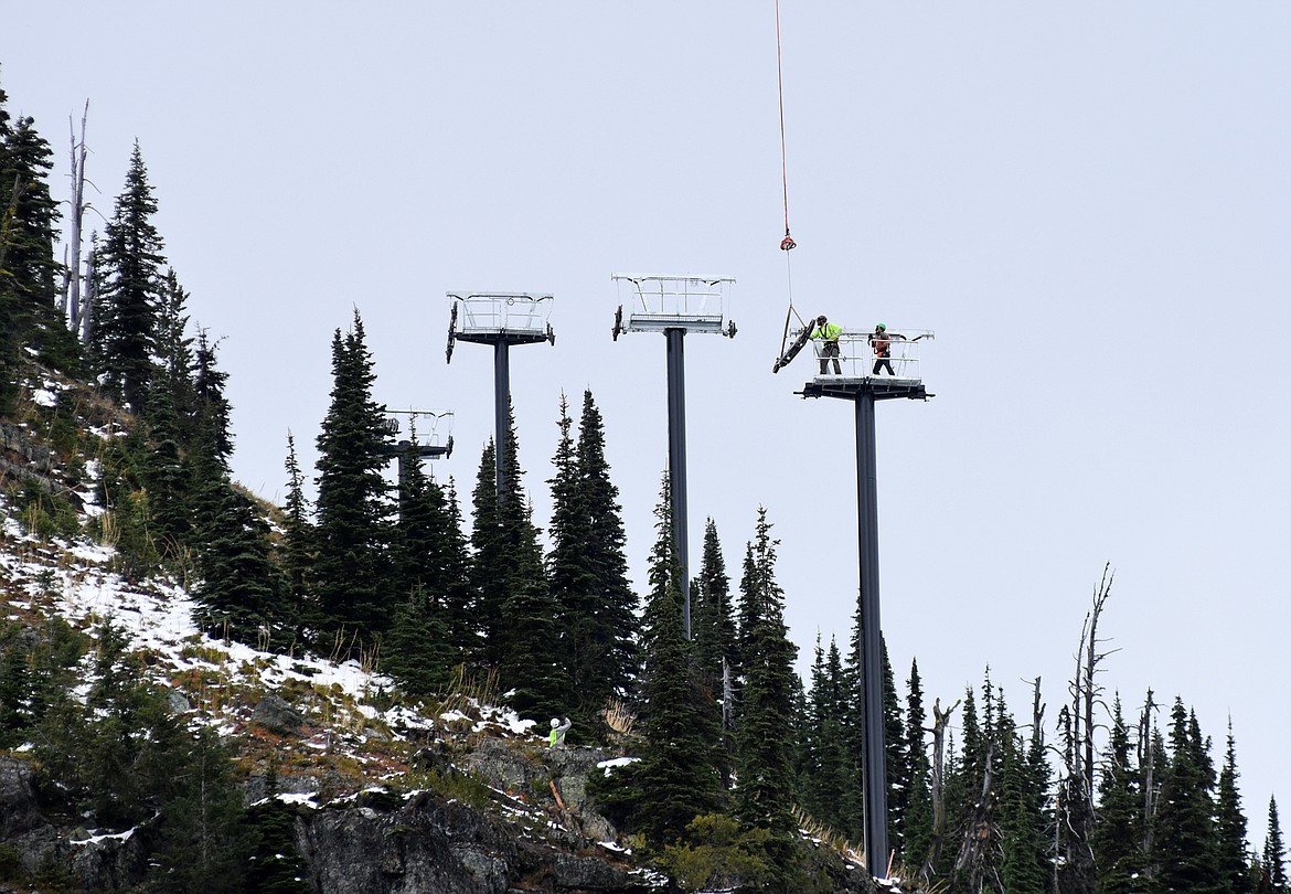 Standing on top of one of the chairlift towers for Chair 5, two crew members grab onto a sheave wheel being delivered by a helicopter. A helicopter Sunday morning flew chairlift towers to the East Rim at Whitefish Mountain resort as part of the relocation of Chair 5 from Ptarmigan Bowl. (Heidi Desch/Whitefish Pilot)