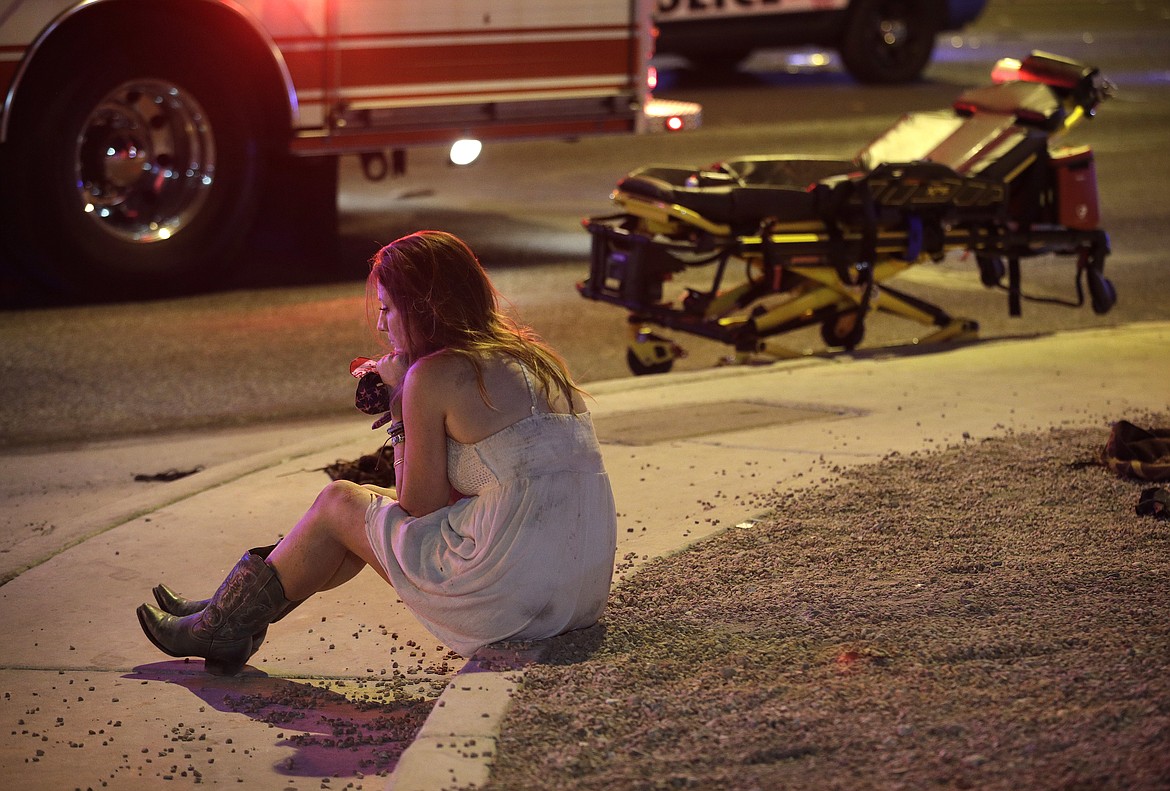 A woman sits on a curb at the scene of a shooting outside of a music festival along the Las Vegas Strip, Monday, Oct. 2, 2017, in Las Vegas. Multiple victims were being transported to hospitals after a shooting late Sunday at a music festival on the Las Vegas Strip. (AP Photo/John Locher)