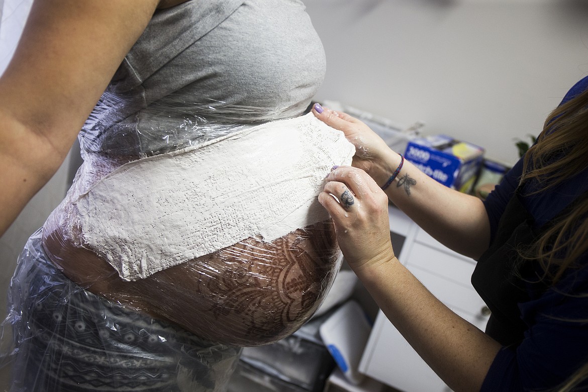 LOREN BENOIT/PressRayne Andrews stretches a plaster strip over Stephanie Dunning's nearly 9-month pregnant belly.