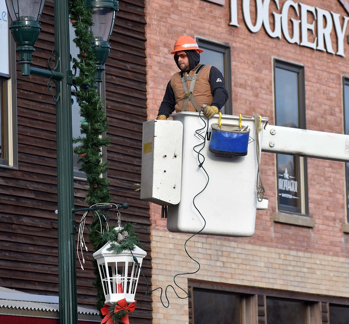 A lineman from Flathead Electric Co-op helps hang the winter decorations Sunday morning on Central Avenue. (Heidi Desch/Whitefish Pilot)