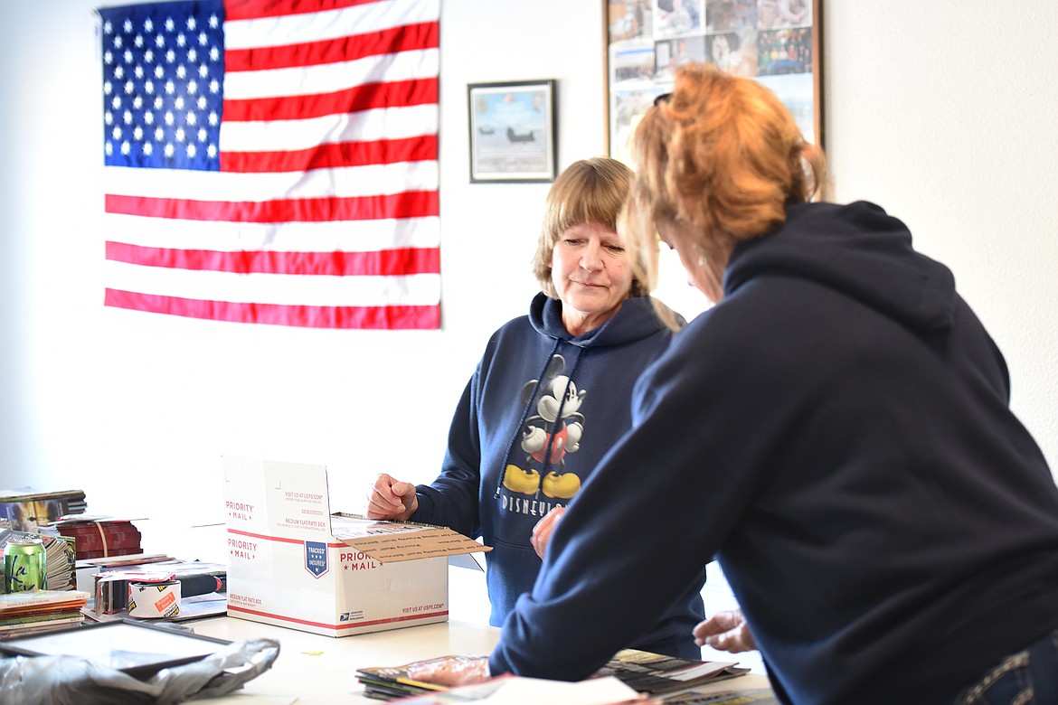 Donna Chase helps box up magazines that will be sent to deployed troops on Tuesday, November 22, in Lakeside.The American Flag in the background was sent to Magazines for Troops by Jeffrey Weathers, a helicopter pilot. It was flown over Afghanistan in 2010. The photos on the wall behind Chase are pictures from deployed troops that have been sent to the organization with the thanks of those receiving the magazines.(Brenda Ahearn/Daily Inter Lake)