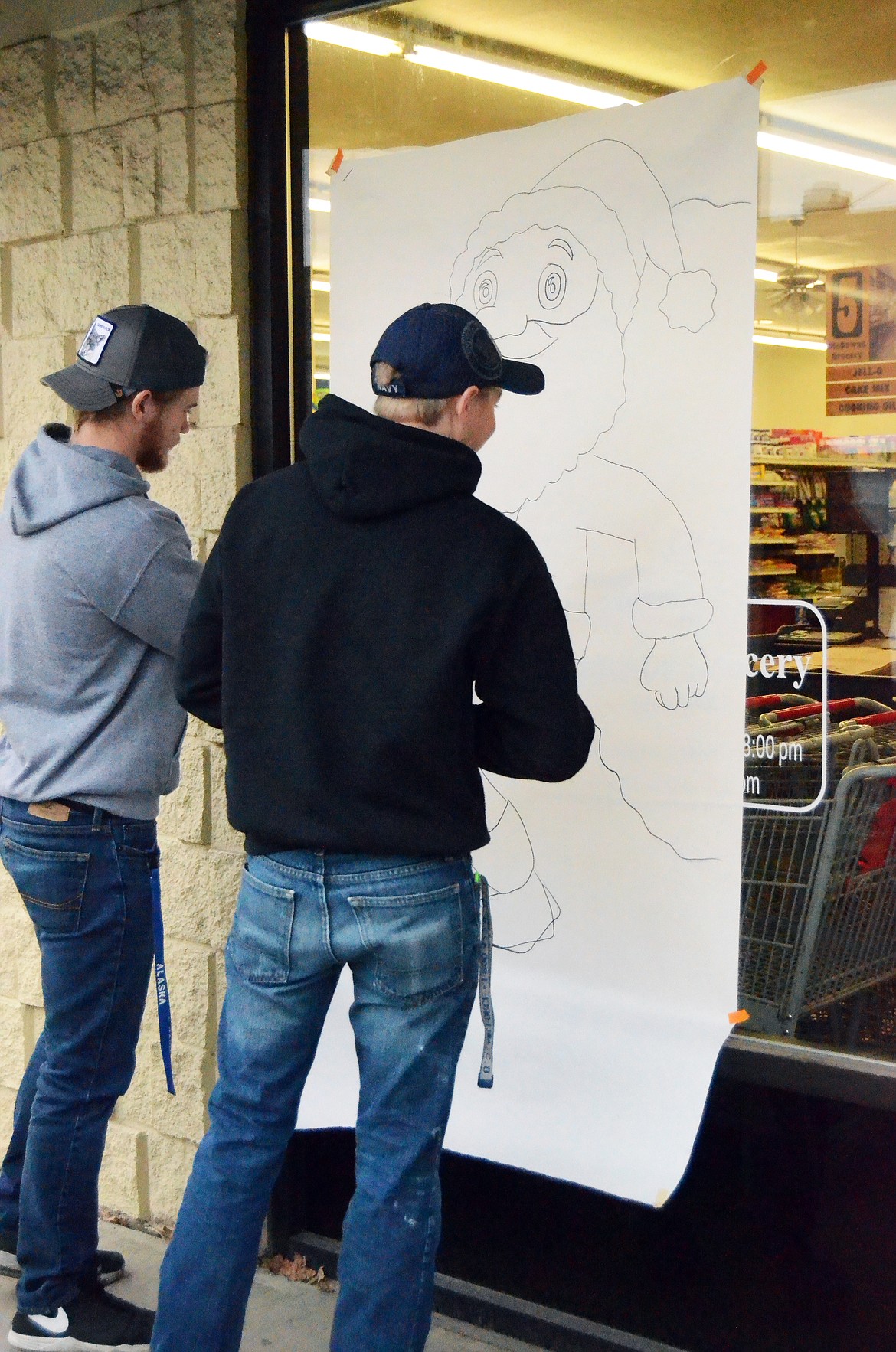 Malachi Paulsen (L) and Austin Safford (R) get prepared to paint a big Santa on the front window of McGowans (Erin Jusseaume/Clark Fork Valley Press)