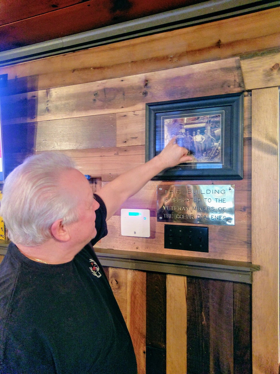 Photo by CHANSE WATSON
The Hilltop&#146;s new owner, Dan Zadra, points to a photo of miners hanging next to the front door and above a plaque that reads &#147;This building is dedicated to the veteran miners of the Coeur d&#146;Alenes.&#148; The photo depicts Dan Albertini, Bart O&#146;Rourke, George Albertini, Laurence Parisotto, Albert Albertini, Jim O&#146;Neal and Paddi McNeal in front of the old Haywire gypo mine in 1920. Zadra is related to the Albertini family, which in the past has owned Albi&#146;s Bar and the Jameson in Wallace. Davy Albertini, 72, still tends bar almost everyday at the Hilltop.