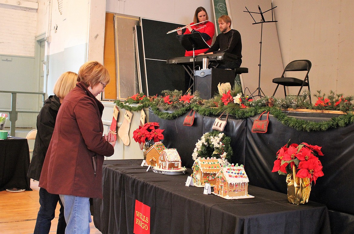 St. Regis music teacher Derek Larson and his wife, Shelly, play holiday music at the Old Schoolhouse Gym for the Wells Fargo Holiday Stroll on Saturday, while shoppers check out the gingerbread houses on display.