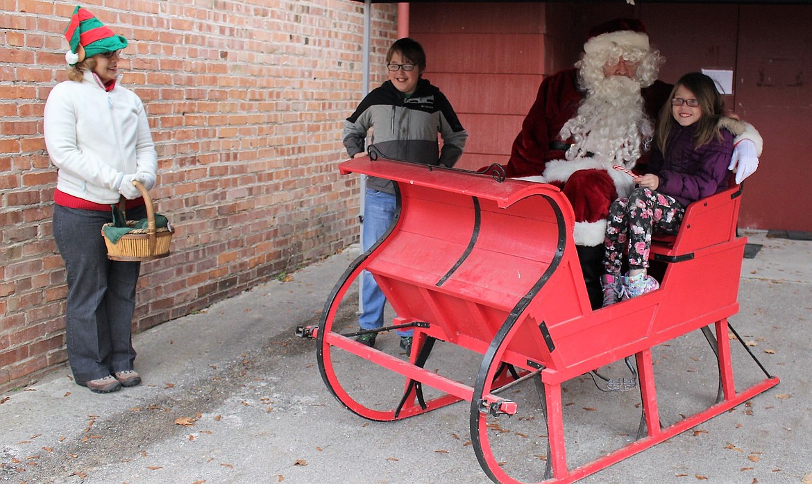 Santa made a visit to the Old Schoolhouse and then to the Mineral County Library craft show at the Superior Elementary School gym. Lilli Webber tells Santa she wants Shopkins, while brother, Devin, asked for video games as Santa&#146;s helper, Loie Turner, looks on. (Kathleen Woodford photos/Mineral Independent)